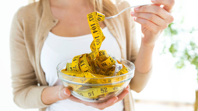Worried cute woman holding bowl with measuring tapes at home.